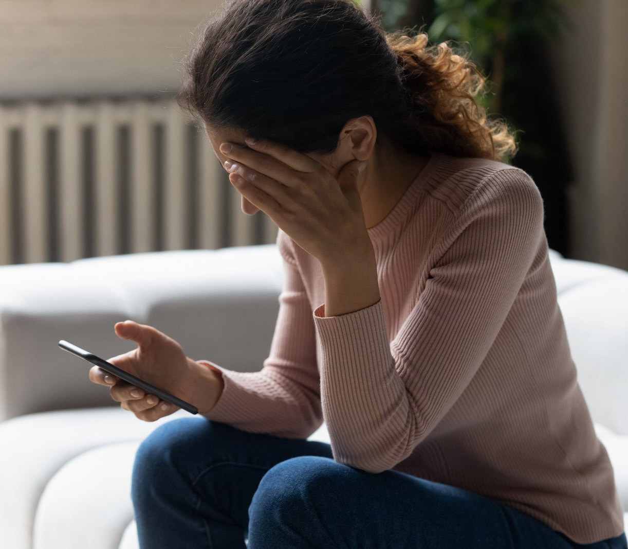 A distressed woman holding a phone while sitting on a couch